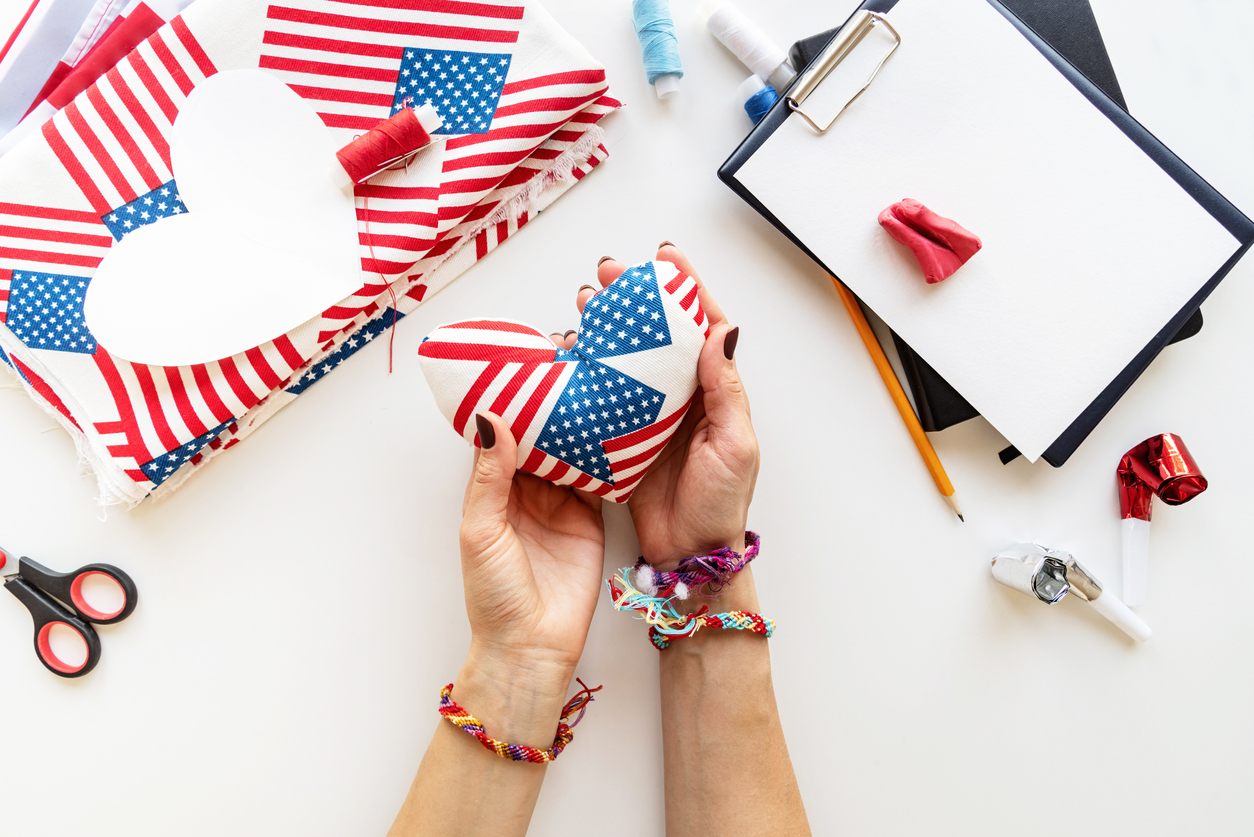 overhead view of woman's hands holding a small heart shaped cushion made from American flag fabric