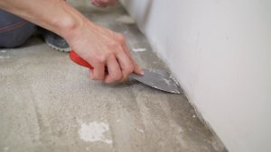 Person scraping paint off concrete floor with a putty knife.