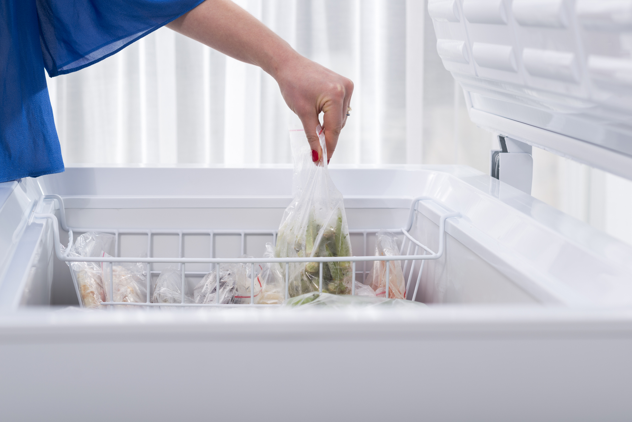 A woman putting some vegetables in the fridge