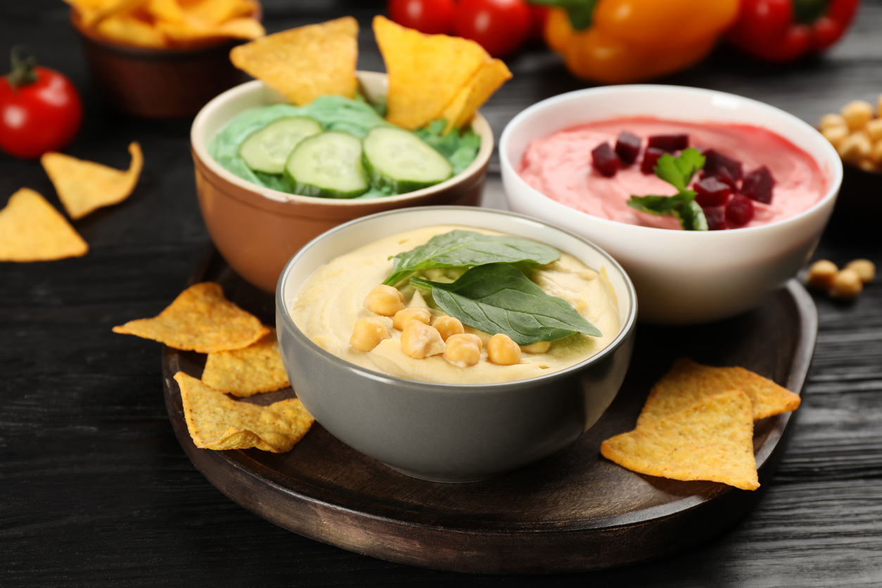 Different kinds of tasty hummus, nachos and ingredients on black wooden table