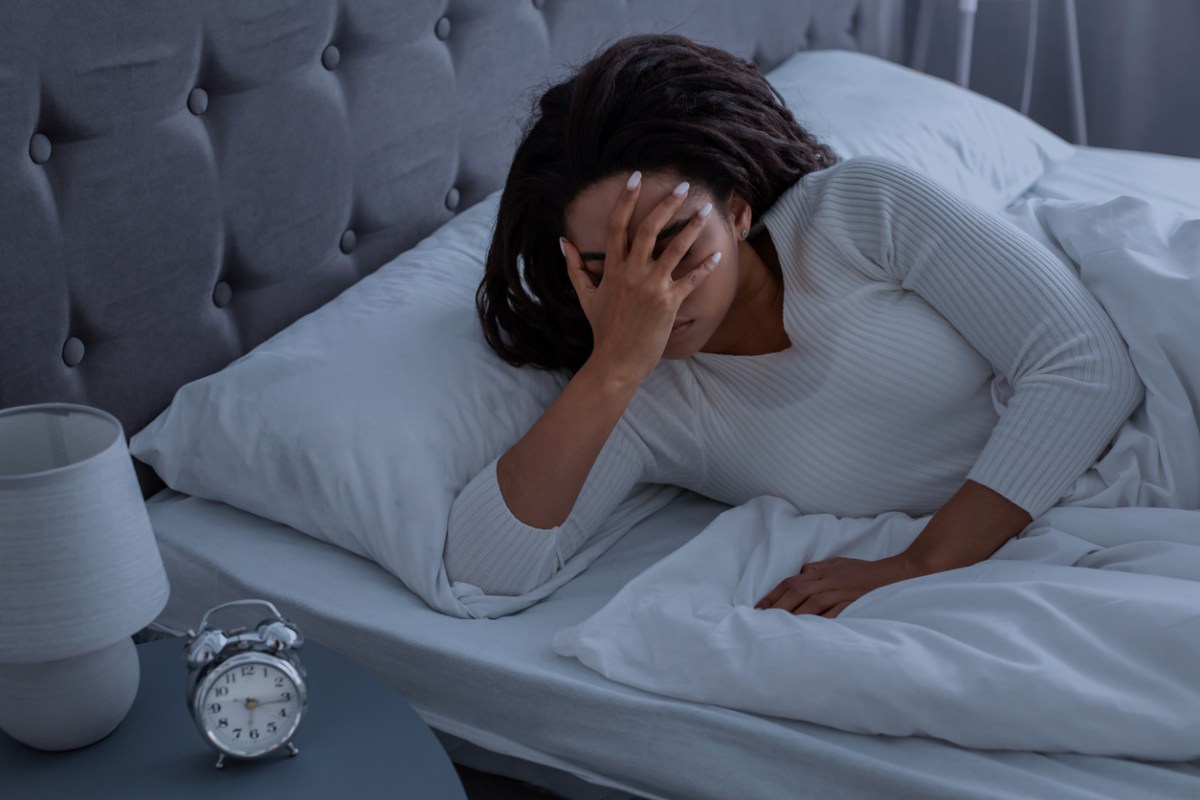 Lack Of Sleep Concept. Stressed young African American woman suffering from insomnia, lying in bed and covering face, waking up throughout the night, feeling depressed about start of the working week
