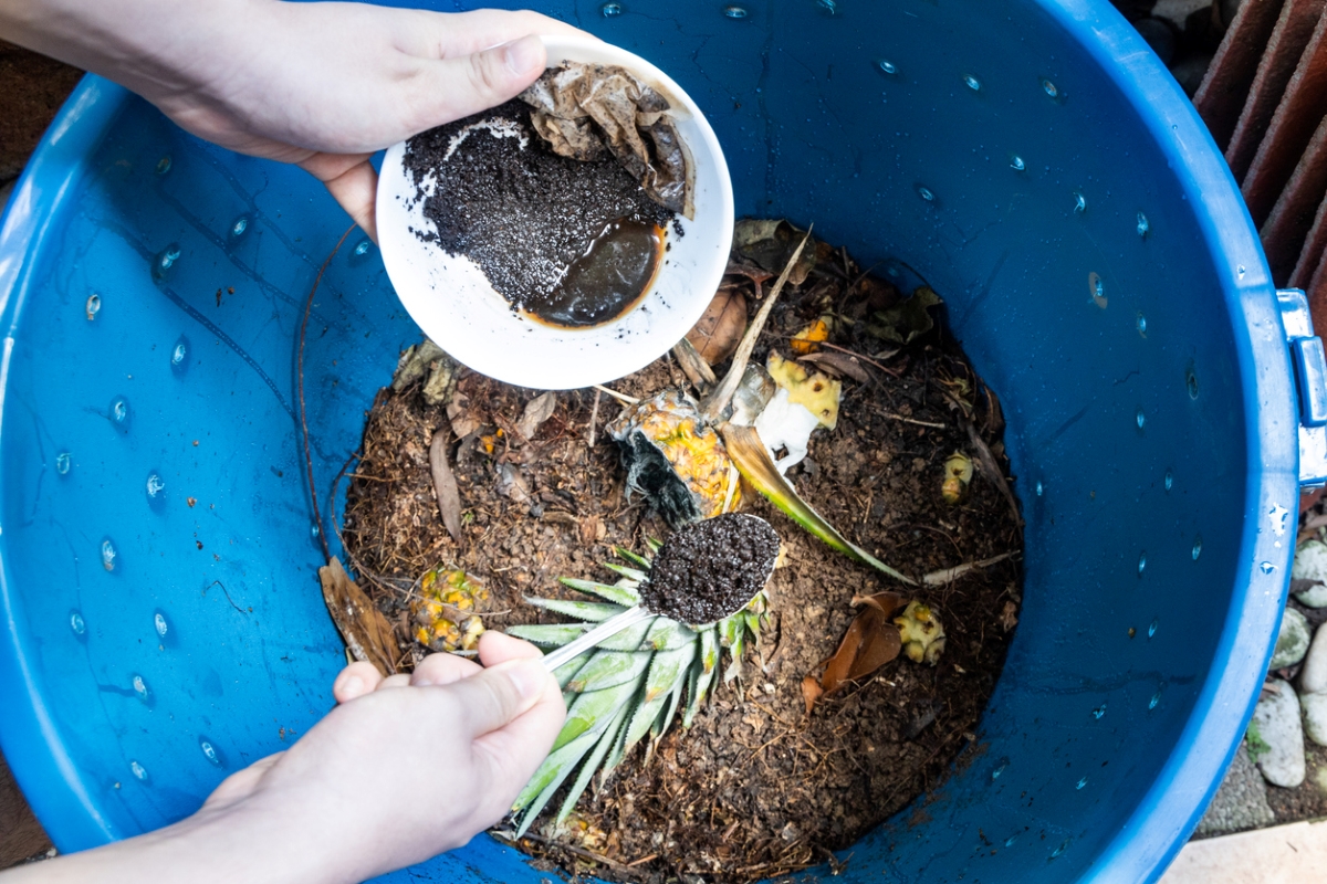 Person adding coffee grounds to compost bin