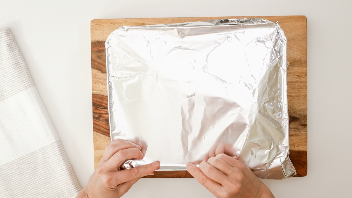 Person using aluminum foil to wrap baking dish