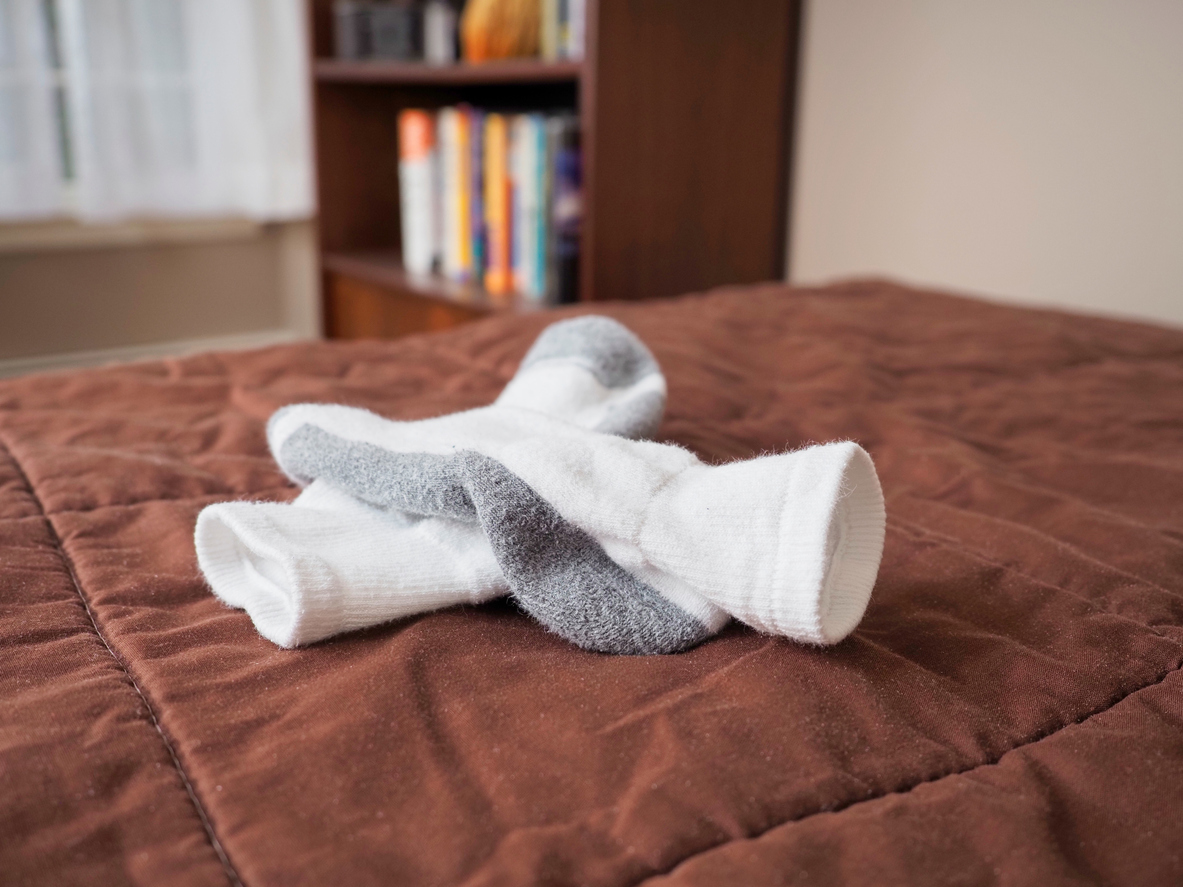 Cold winter weather may require socks worn to bed to keep your feet warm, a wintertime concept. White socks sit atop a brown quilt on a bed in a domestic bedroom. Other bedroom furnishings remain blurred in background including a bookcase.