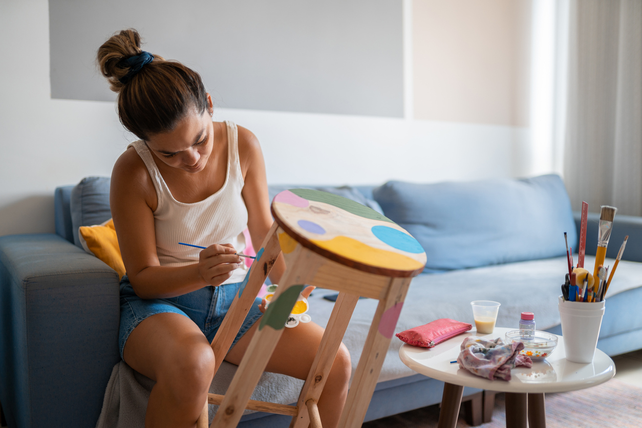young woman in living room painting a wooden stool with several colors