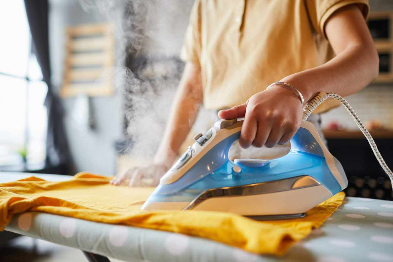 woman ironing yellow shirt on ironing board