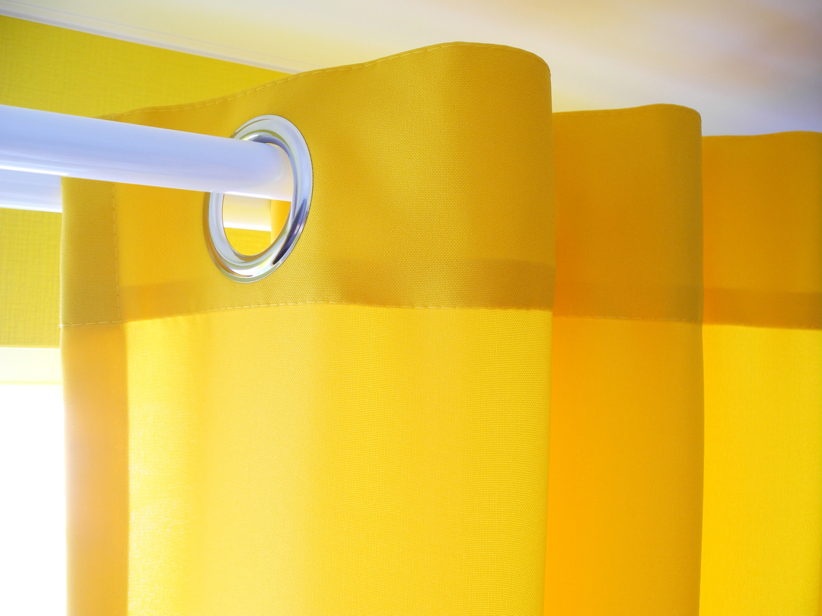 Bright solid yellow curtain with grommets or eyelets close-up, modern interior design in vibrant colors