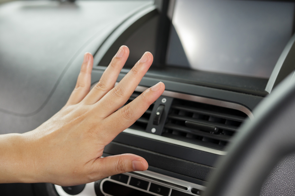 person feeling for car air conditioner temperature with hand in front of vents