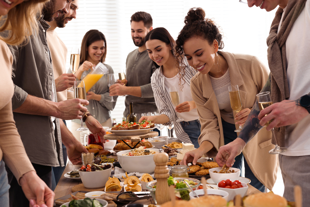 group-of-young-people-hold-champagne-glasses-and-serve-themselves-at-a-potluck-buffet
