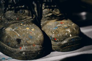 Black suede shoes with paint splatters on them.