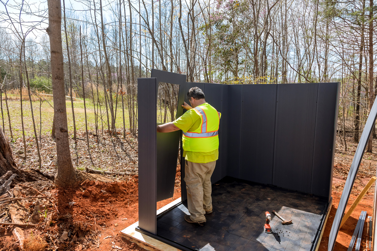 man-in-a-yellow-safety-vest-assembles-a-shed-in-front-of-trees