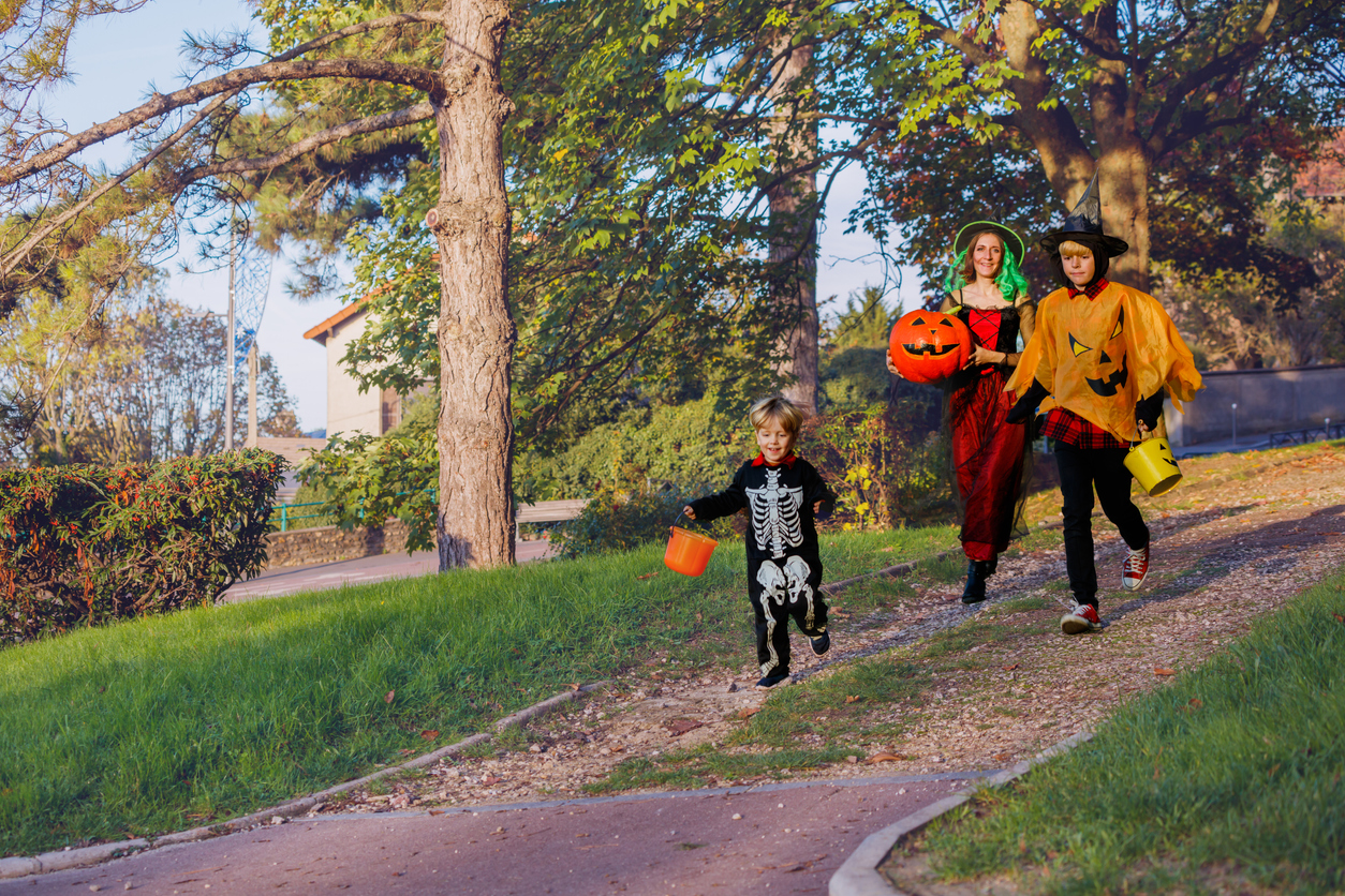Family with brother boys run in Halloween disguise hold bucket for candies over the town park
