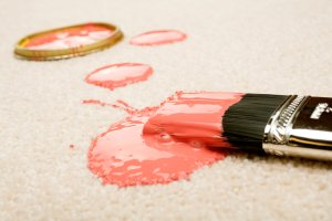 Paintbrush with reddish paint drips onto an ivory-colored carpet.