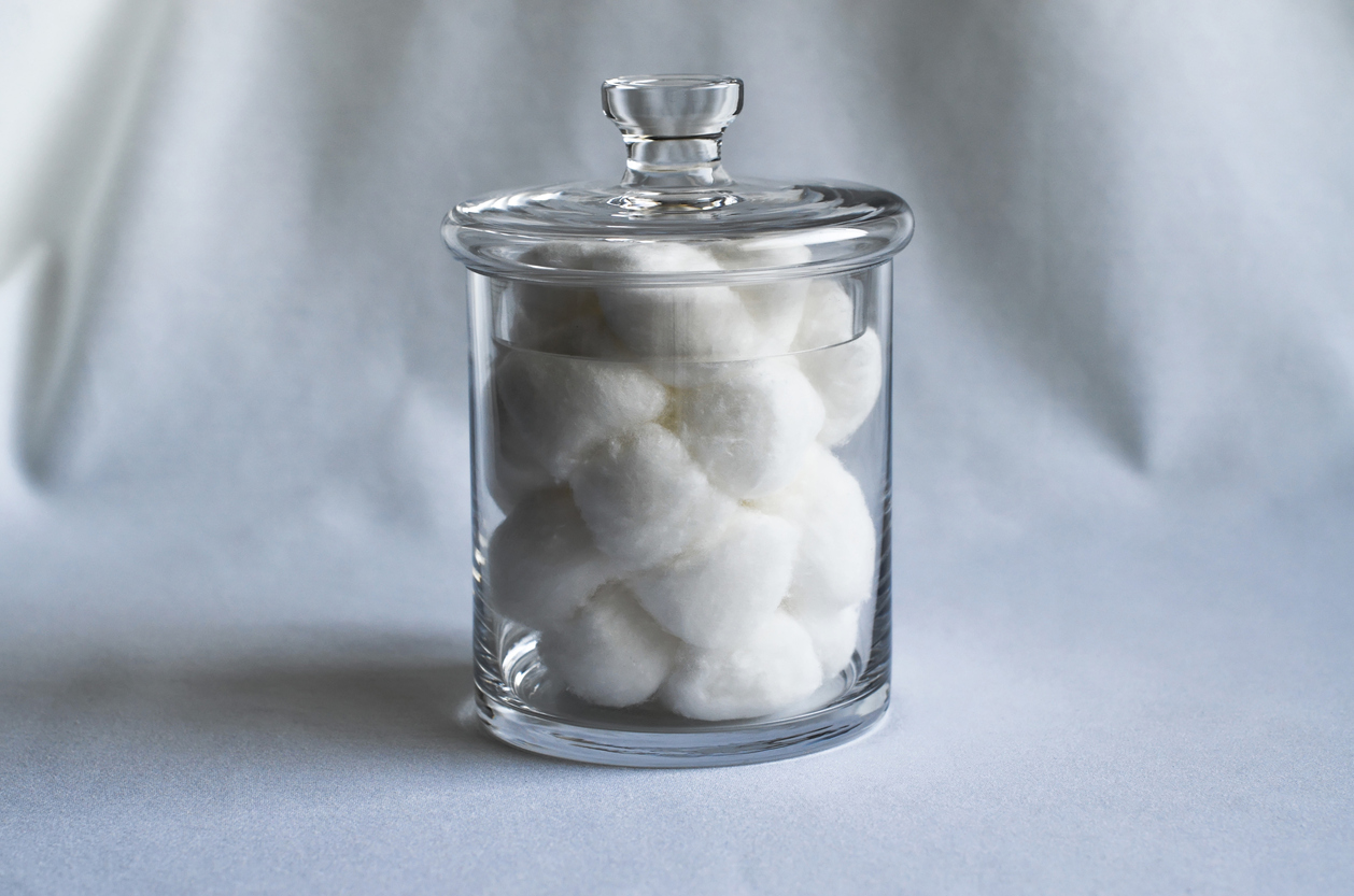 Cotton balls in glass jar on a white sheet.