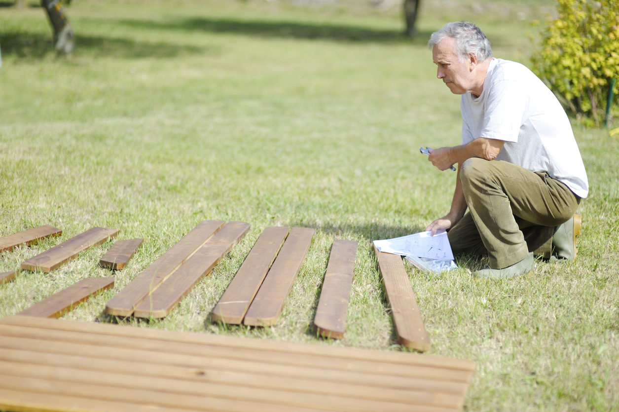 senior-man-holds-instructions-while-building-a-storage-shed-in-his-yard