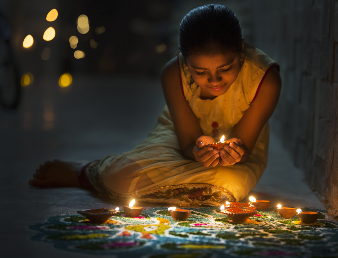 a-girl-holds-a-lit-diya-and-sets-it-down-on-a-rangoli-for-diwali-celebration