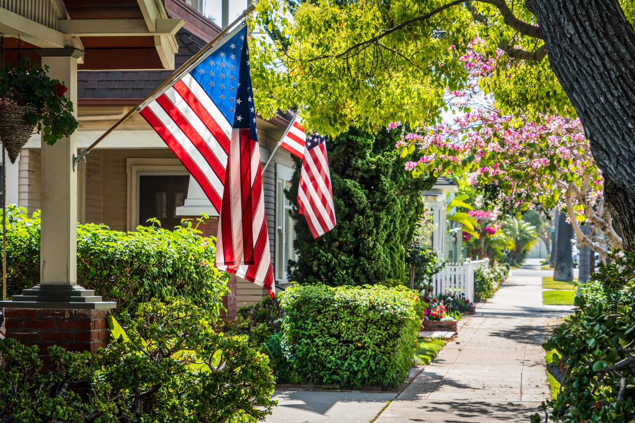 residential street with trees and two American Flags hanging from neighboring houses