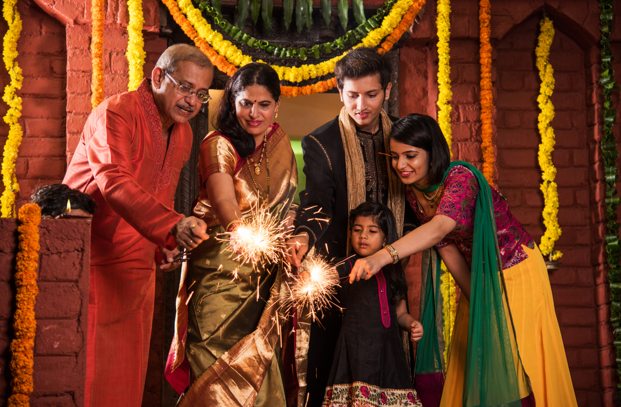 family-holds-sparklers-together-in-front-of-Diwali-decorations-and-marigold-garlands