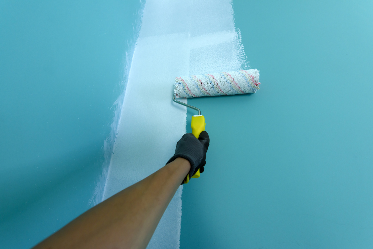 hand rolling white paint with a paint roller onto a green wall