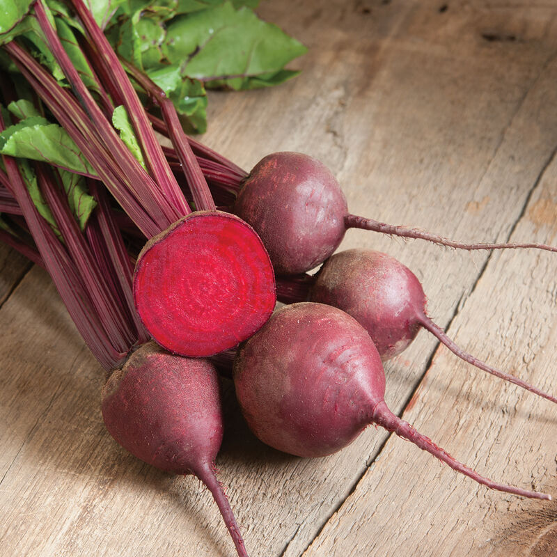 group of beets on wooden table with one beet sliced in half showing the bright red inside