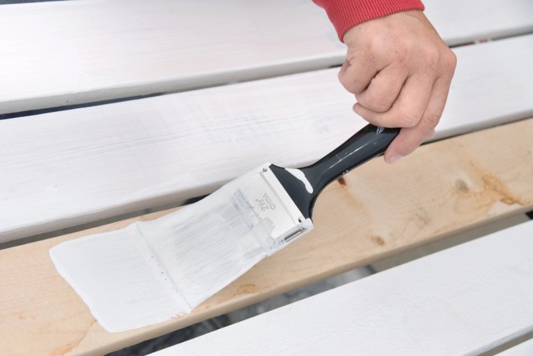 A painter primes the wooden slats of a natural wood fence.
