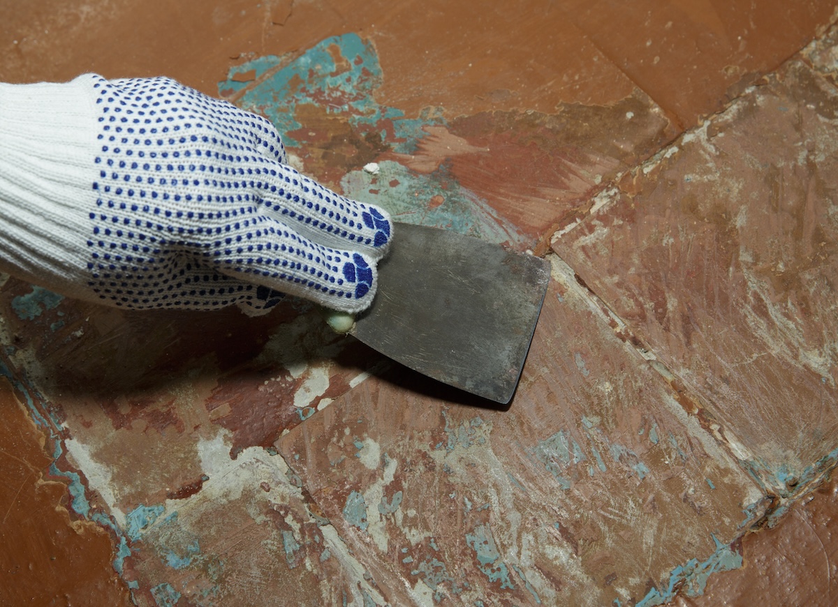 Pearson wearing a work glove removes old paint from the tile with a putty knife.
