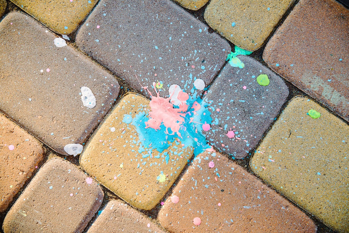 Dribbles of blue, white, and pink paint on brick paving slabs.