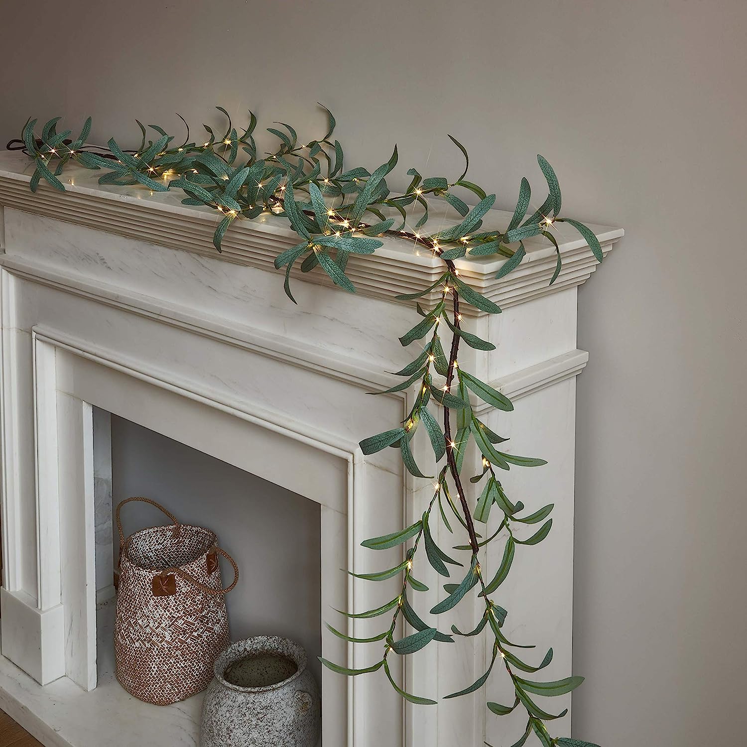 An-olive-leaf-string-of-lights-decorates-a-white-fireplace-mantel.