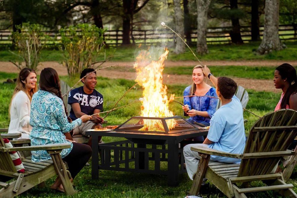 A group of people gathered around a cheap fire pit while smiling and roasting marshmallows.
