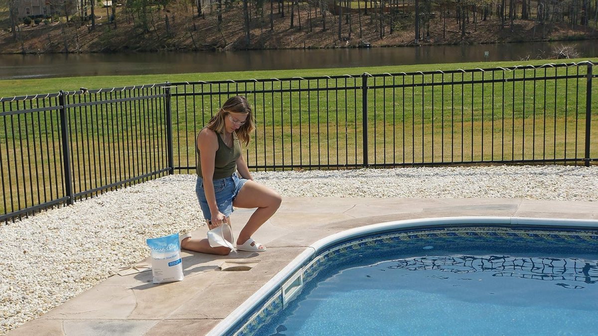 A person kneeling by a pool to add the best pool stabilizer option to the water