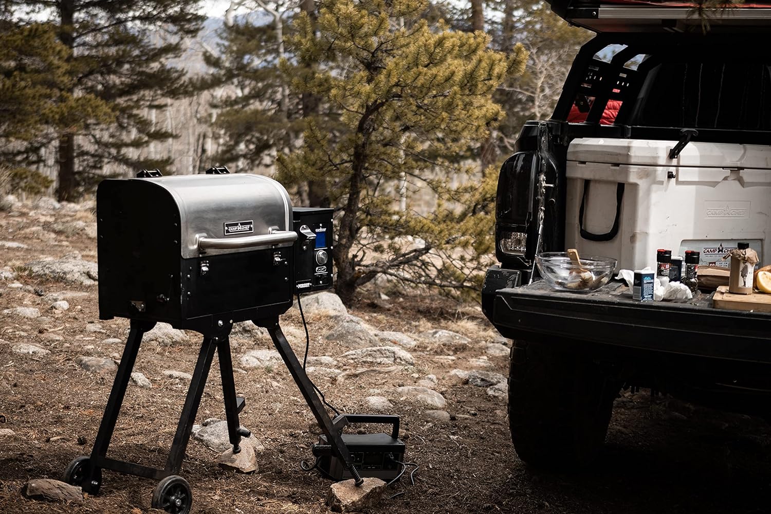 The best portable pellet grill option set up in a wooded area next to a pickup truck bed