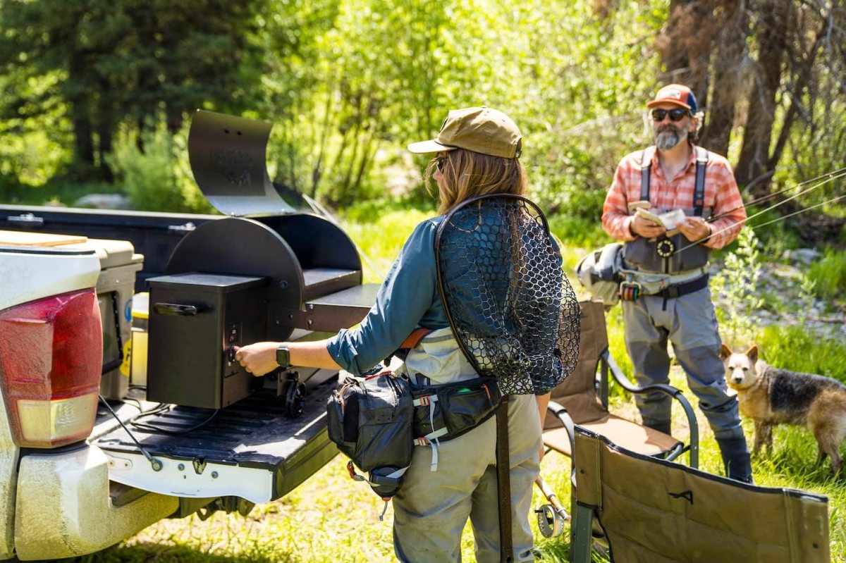 A person with a fishing net using the best portable pellet grill option in an outdoor wooded setting
