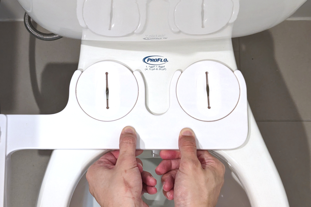 A person using both hands to lower a Tushy Classic bidet onto a two-piece toilet bowl with the seat removed