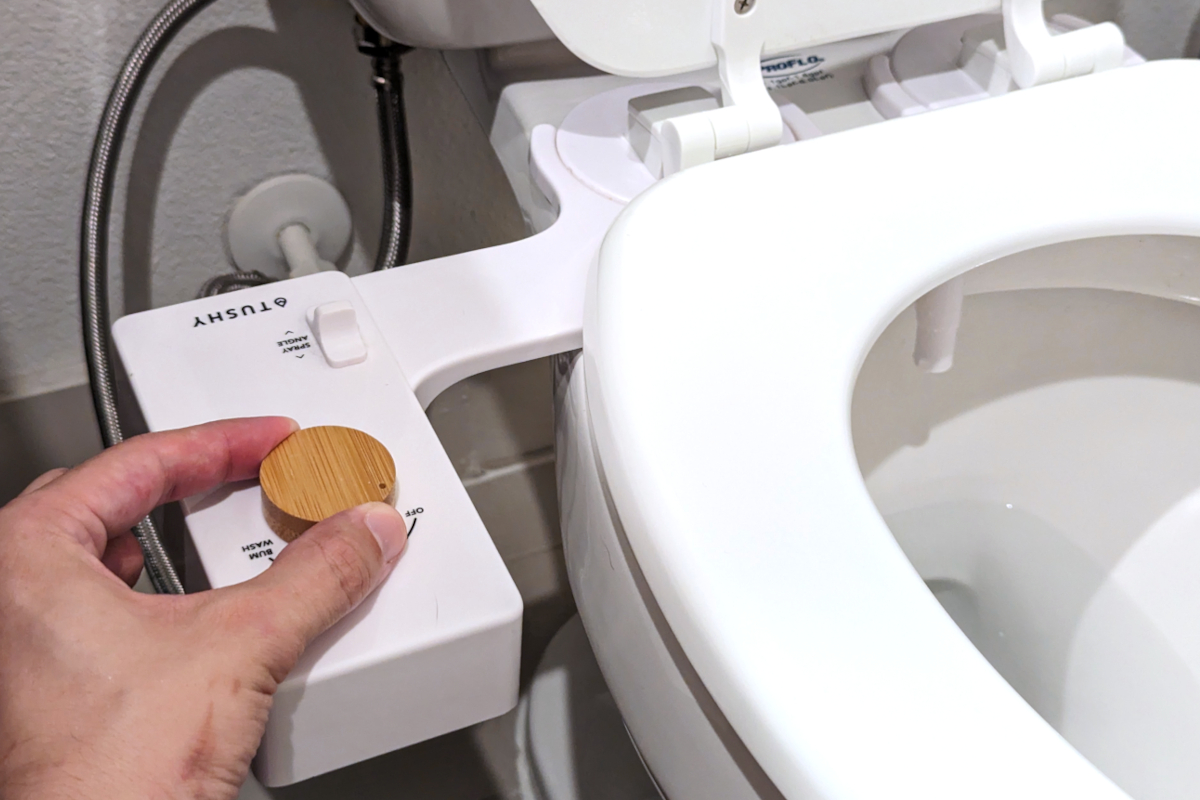 A person testing the bamboo spray control of a Tushy Classic bidet attachment.