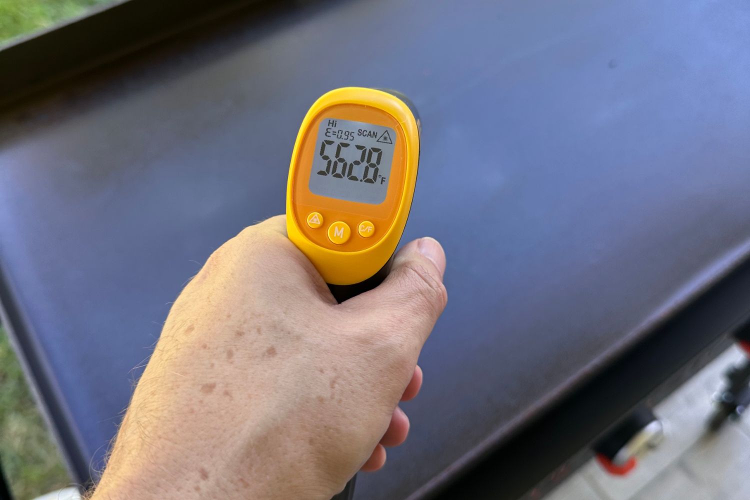 Person measuring the surface temperature of a griddle with yellow infrared thermometer.