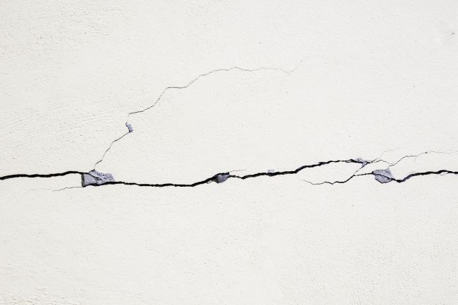 Cracks in a white wall are seen close up.