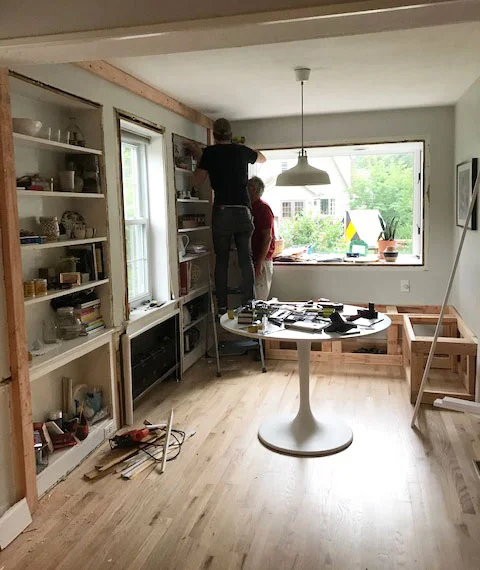 Two people work on the renovation of a breakfast nook with built-in shelves and a tulip table.