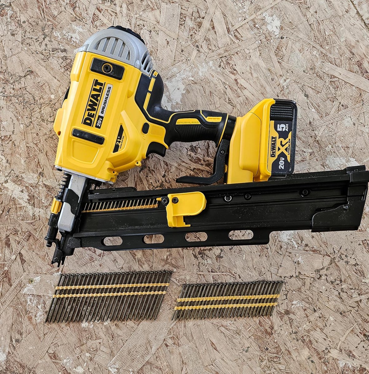 DeWalt Cordless Framing Nailer resting on its side on plywood next to a full cartridge of nails.