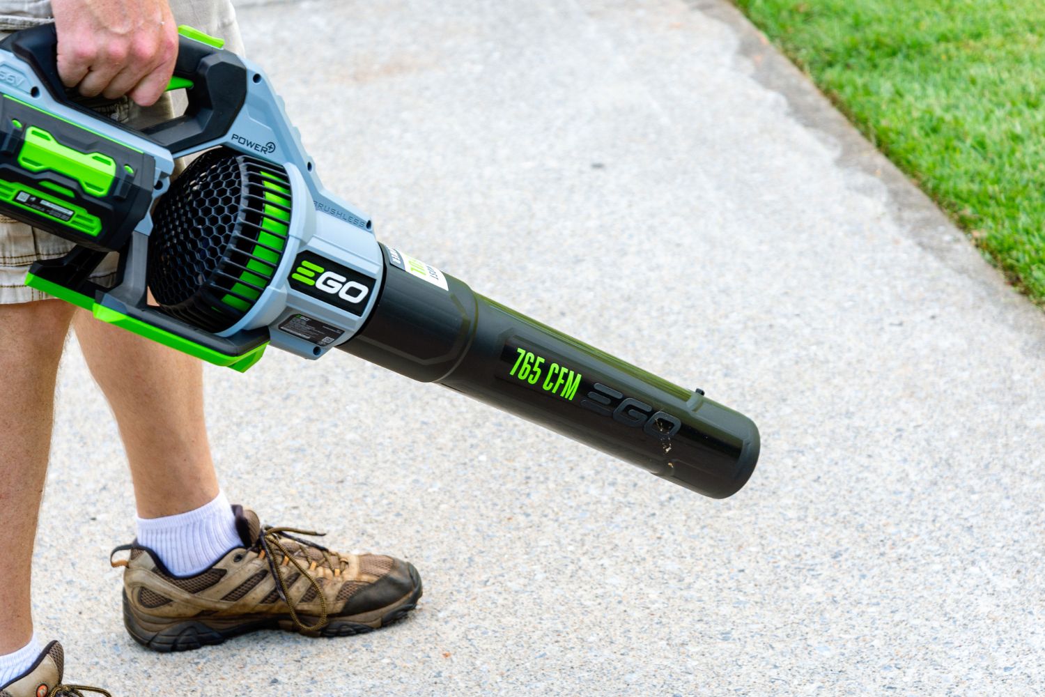 A person using the Ego Power+ 650 CFM 56V Leaf Blower to clear debris from a sidewalk.