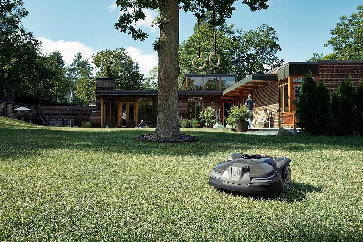 A Husqvarna robotic lawn mower on a large green lawn with a spacious home in the background.
