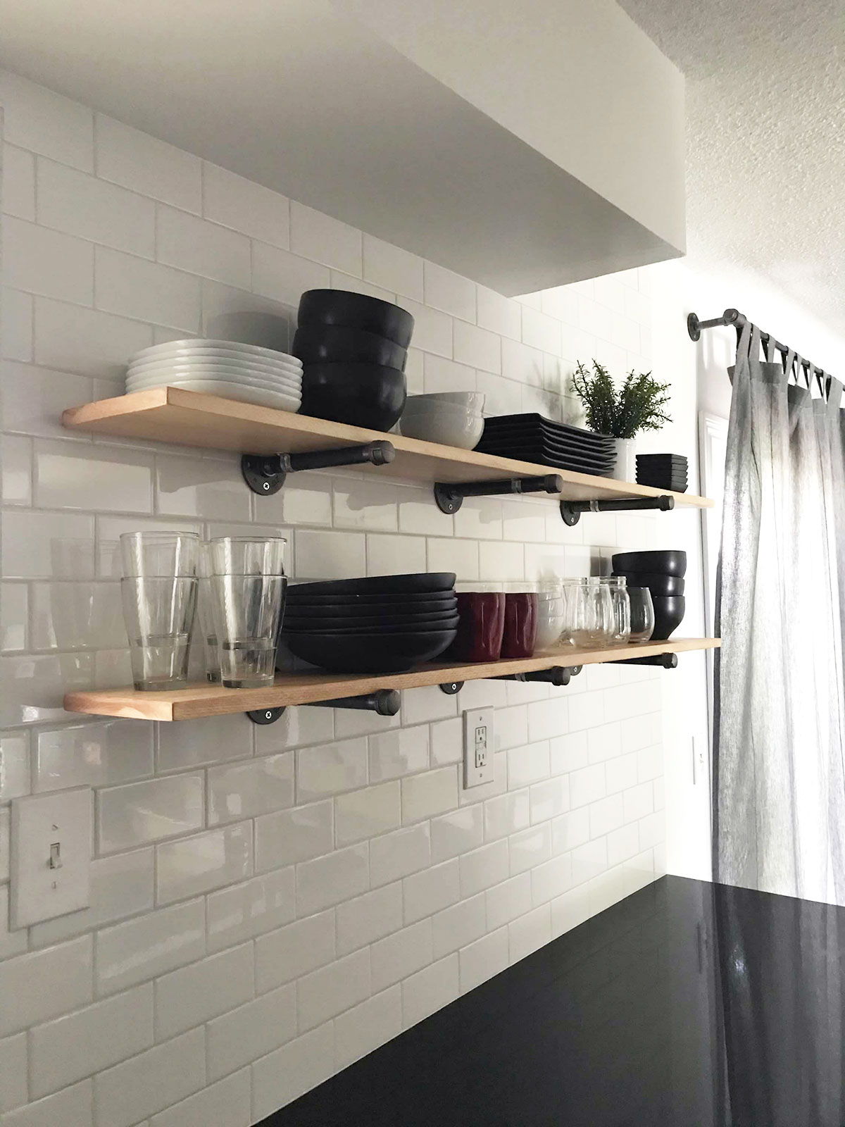 Two open shelves against a white tile backsplash hold a display of black and white dishes.