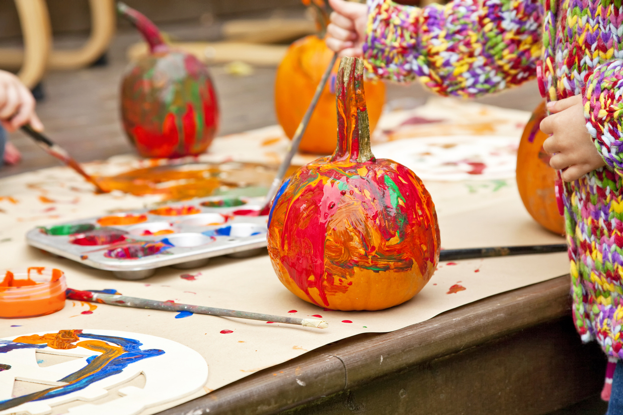 Young children painting small pumpkins an assortment of colors on an outdoor deck.