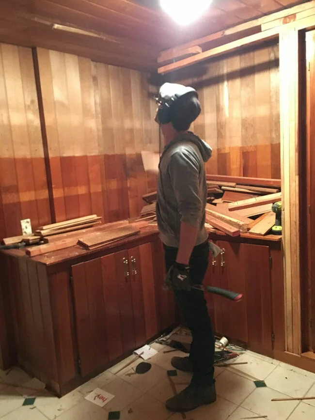 A person looks at ongoing renovation work in a wood paneled area that will become a mudroom.