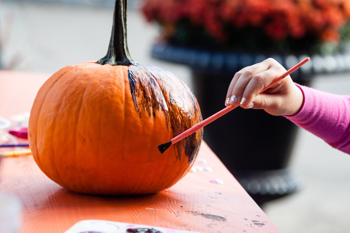A young girl painting a medium-size pumpkin black with a watercolor brush.