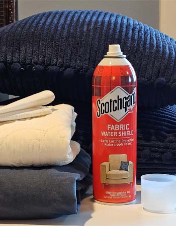 The Scotchgard Fabric Protector on a table next to an array of fabric, including sheets and upholstery.