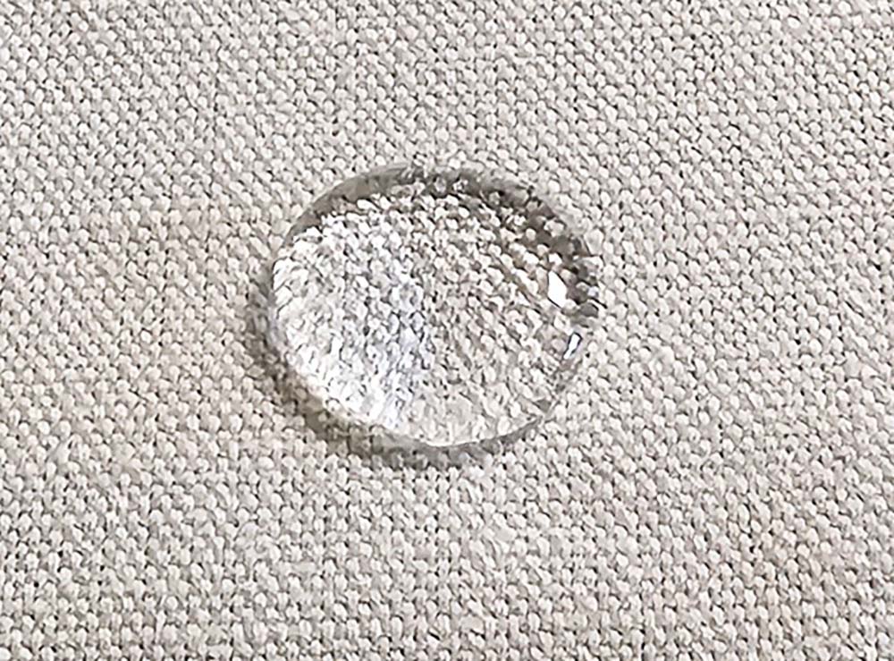 A large drop of water sitting on upholstery that's been treated with Scotchgard fabric protector and not absorbing into the material.