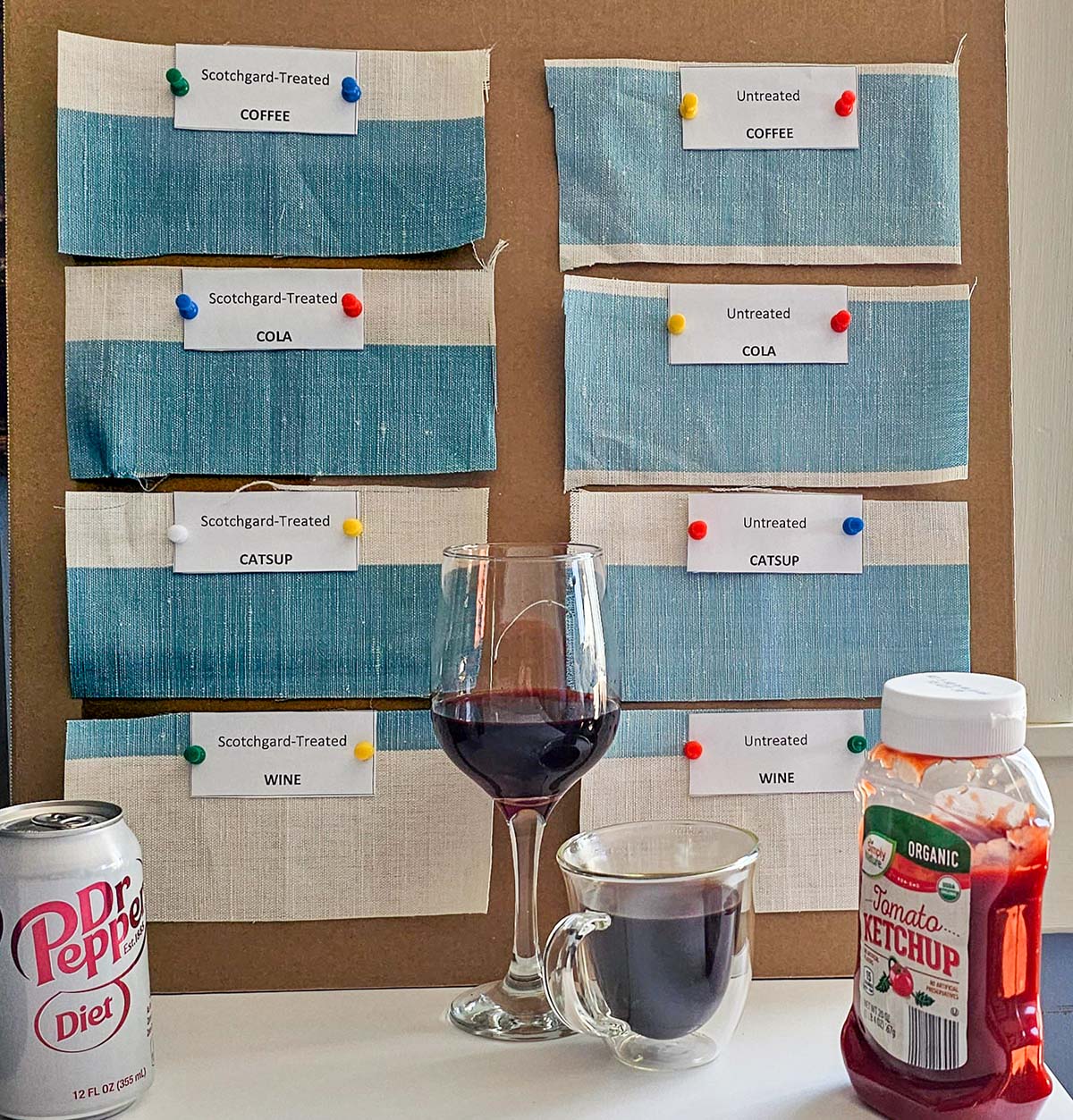 A test board of fabric swatches treated and untreated with Scotchgard fabric protector with several stain-causing substances in the foreground.