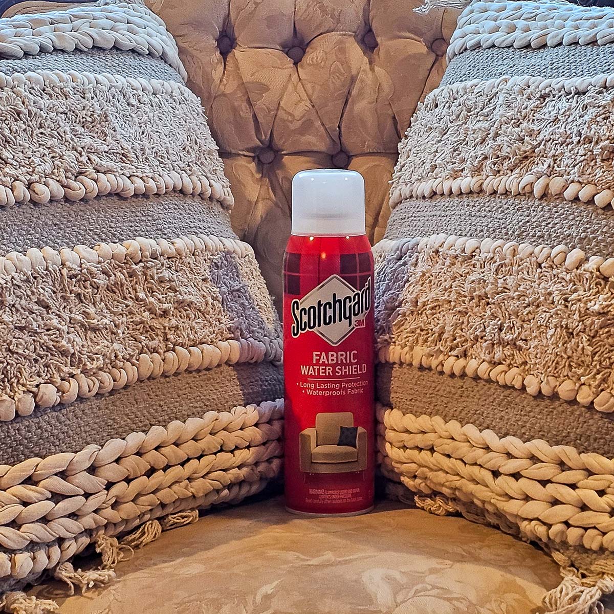A can of Scotchgard fabric protector sitting on a couch between two throw pillows.