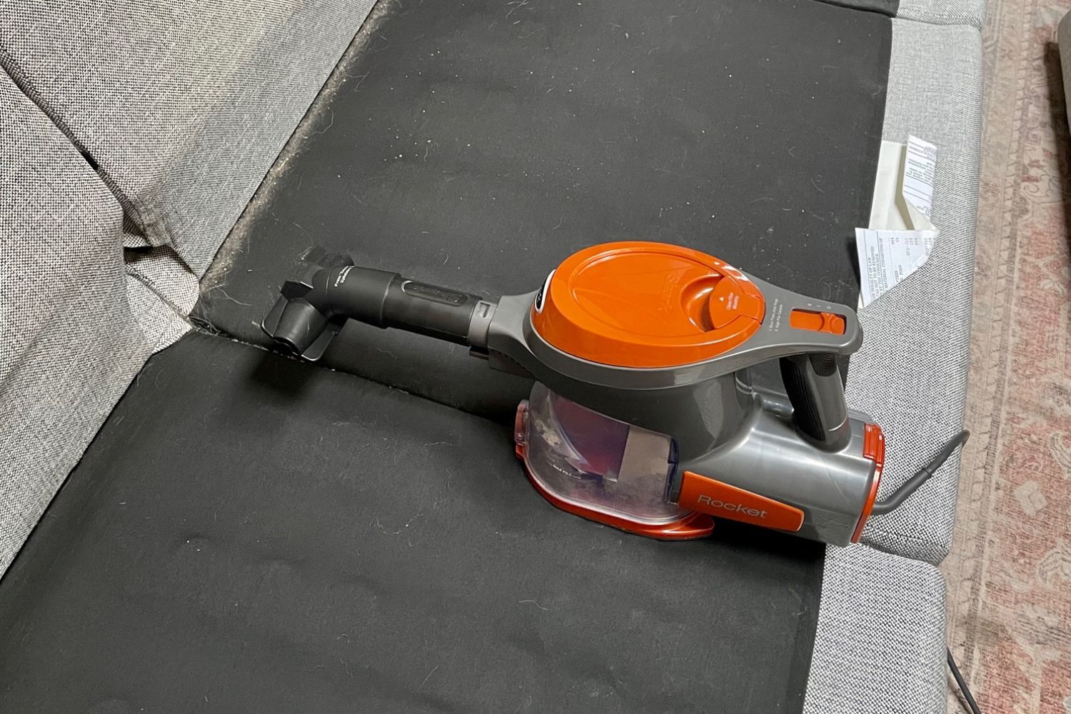 Shark Rocket vacuum in handheld configuration cleaning underneath gray couch cushions.