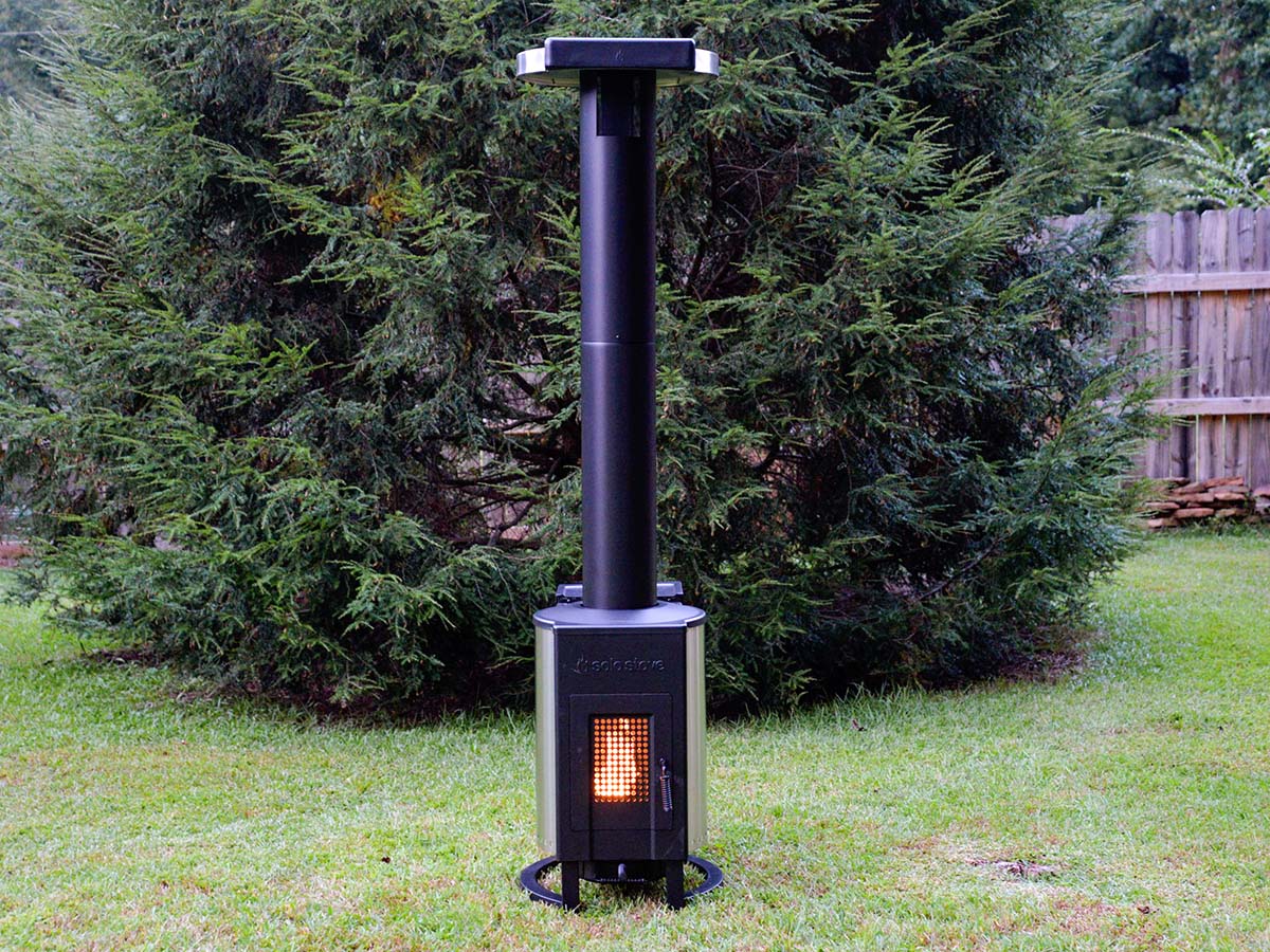 Tall, black Solo Stove Tower Patio Heater on lawn in front of evergreen tree.